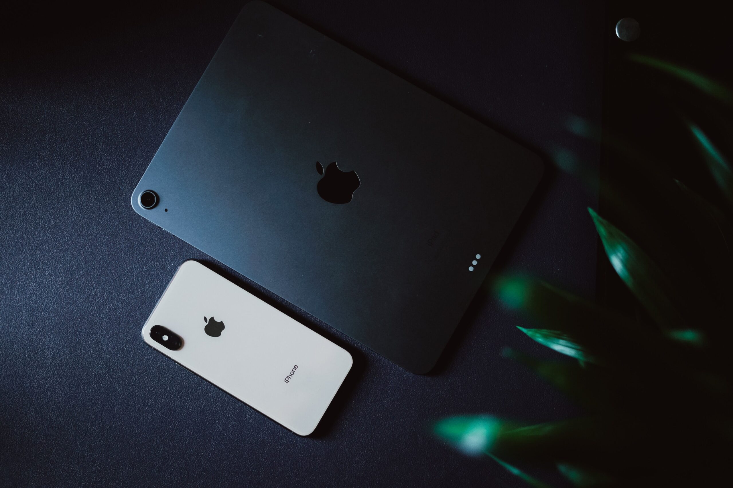 Modern gadgets including an iPhone and iPad placed on a black surface with a moody aesthetic.